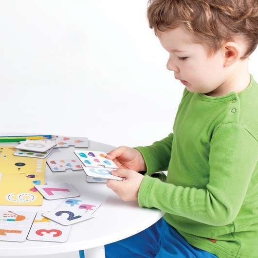 A little boy in a green shirt is playing with numbers on a table