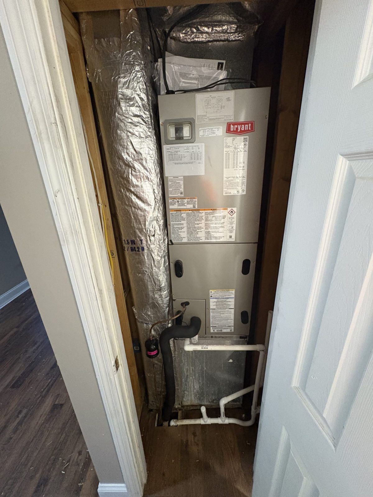 HVAC unit in a closet. Silver and gray metal, with ductwork. White door and wood trim.