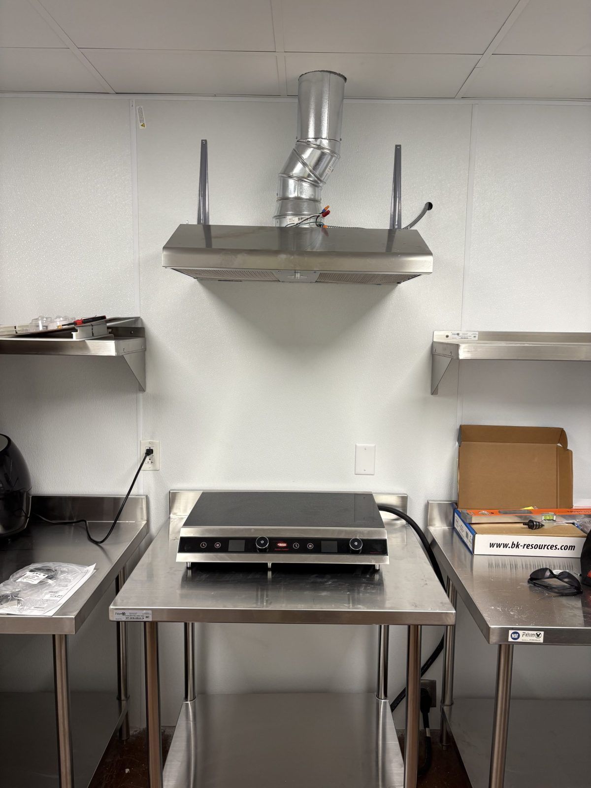 Stainless steel kitchen with a stove, hood, and shelving.