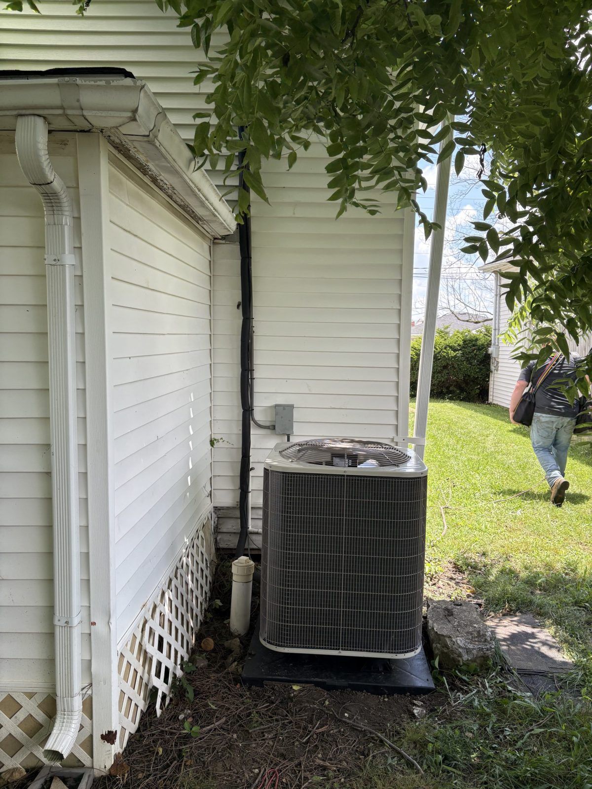 An air conditioning unit next to a white house with a person walking away in a yard.