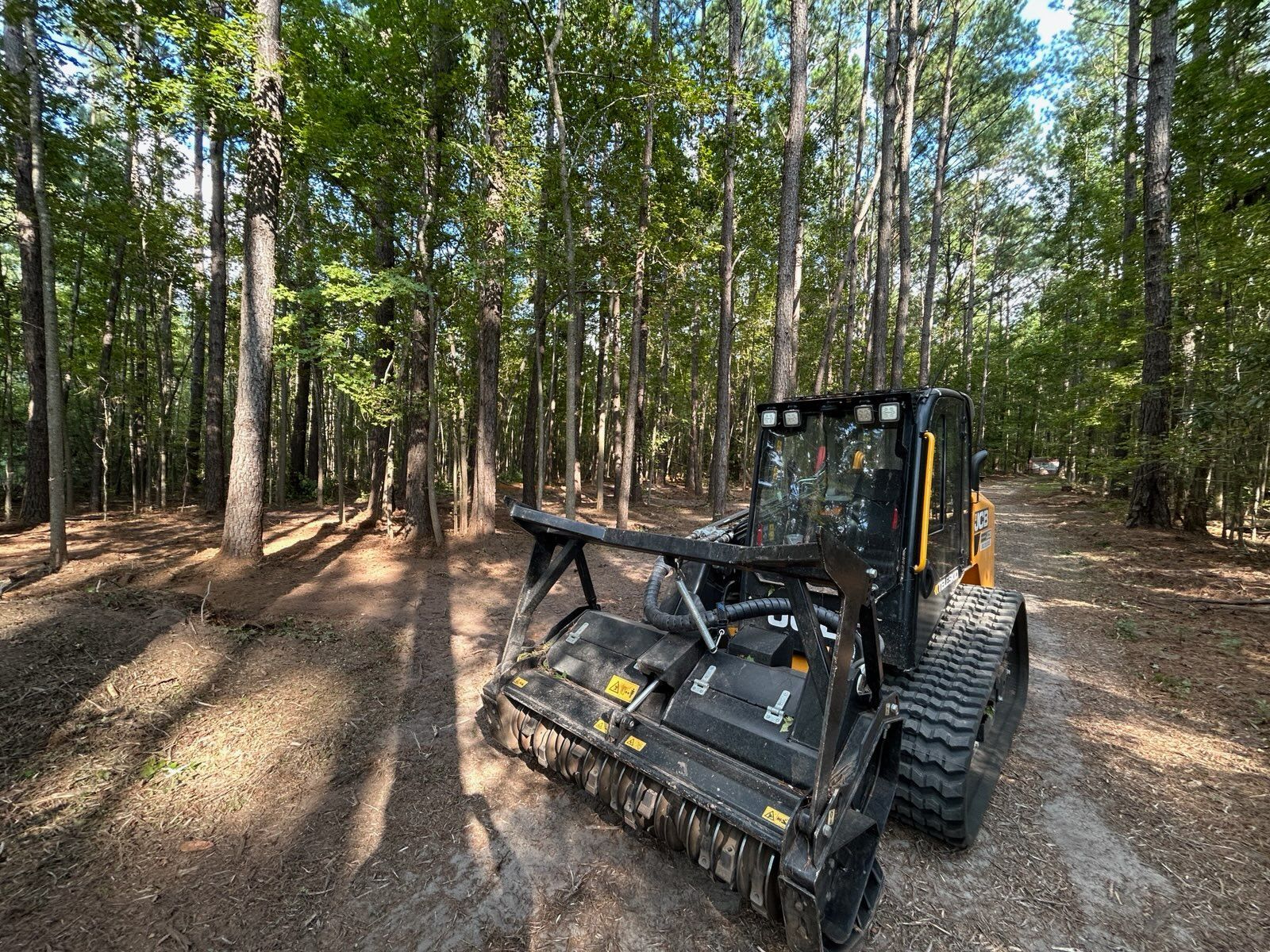 A mulching machine on a path in a forest clearing, cutting vegetation.