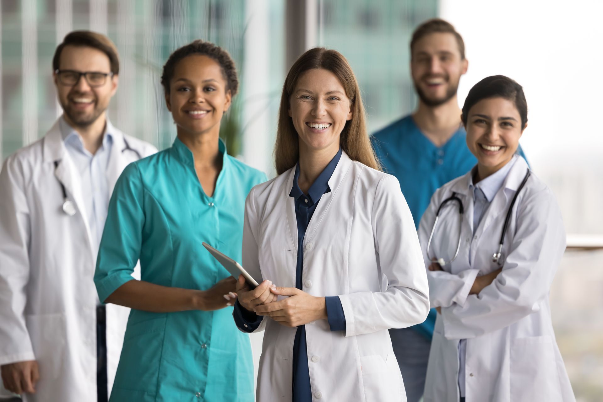 Medical team of five smiling at camera. Doctors and nurses in scrubs and lab coats.