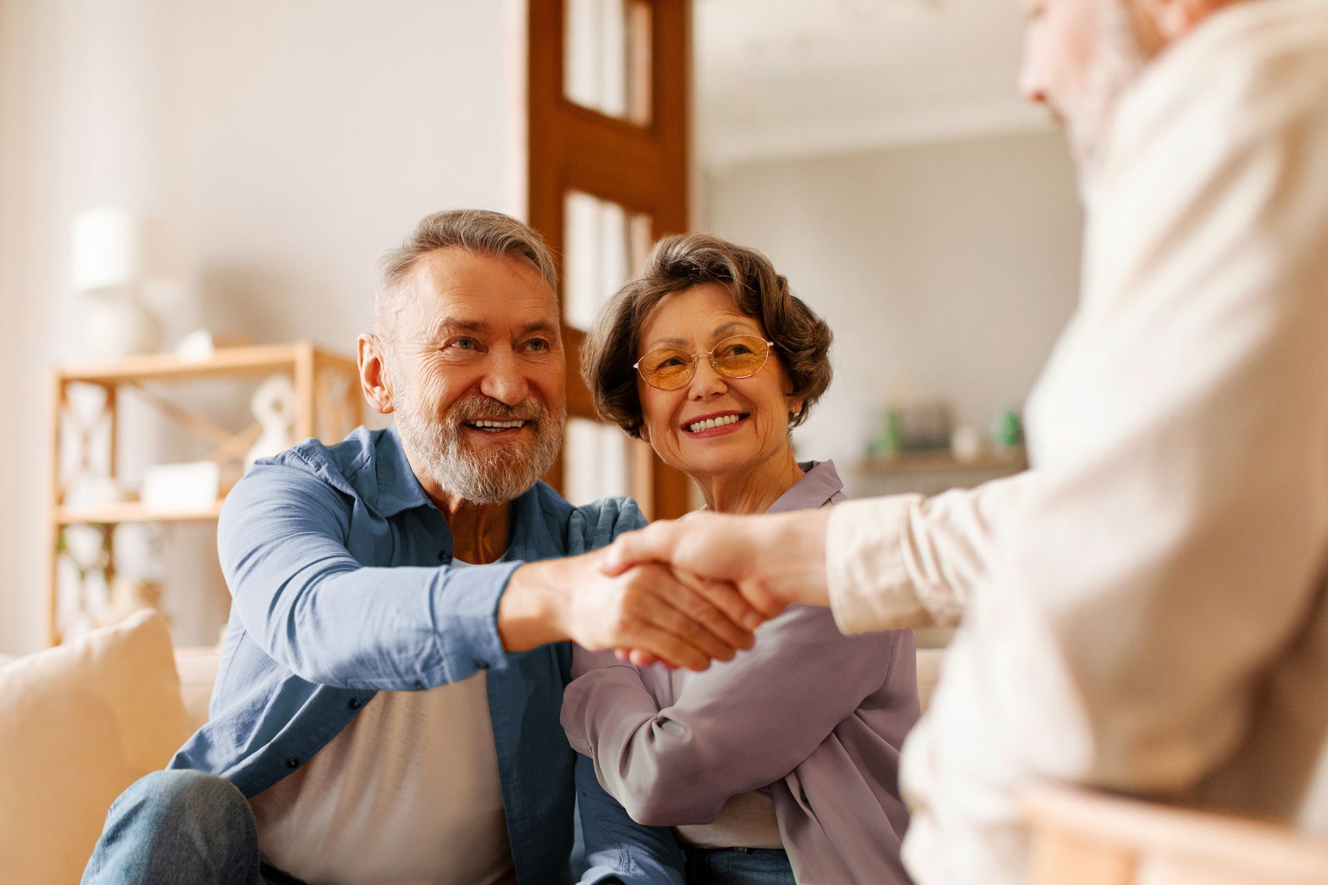 Older couple shaking hands with another person; smiling indoors.