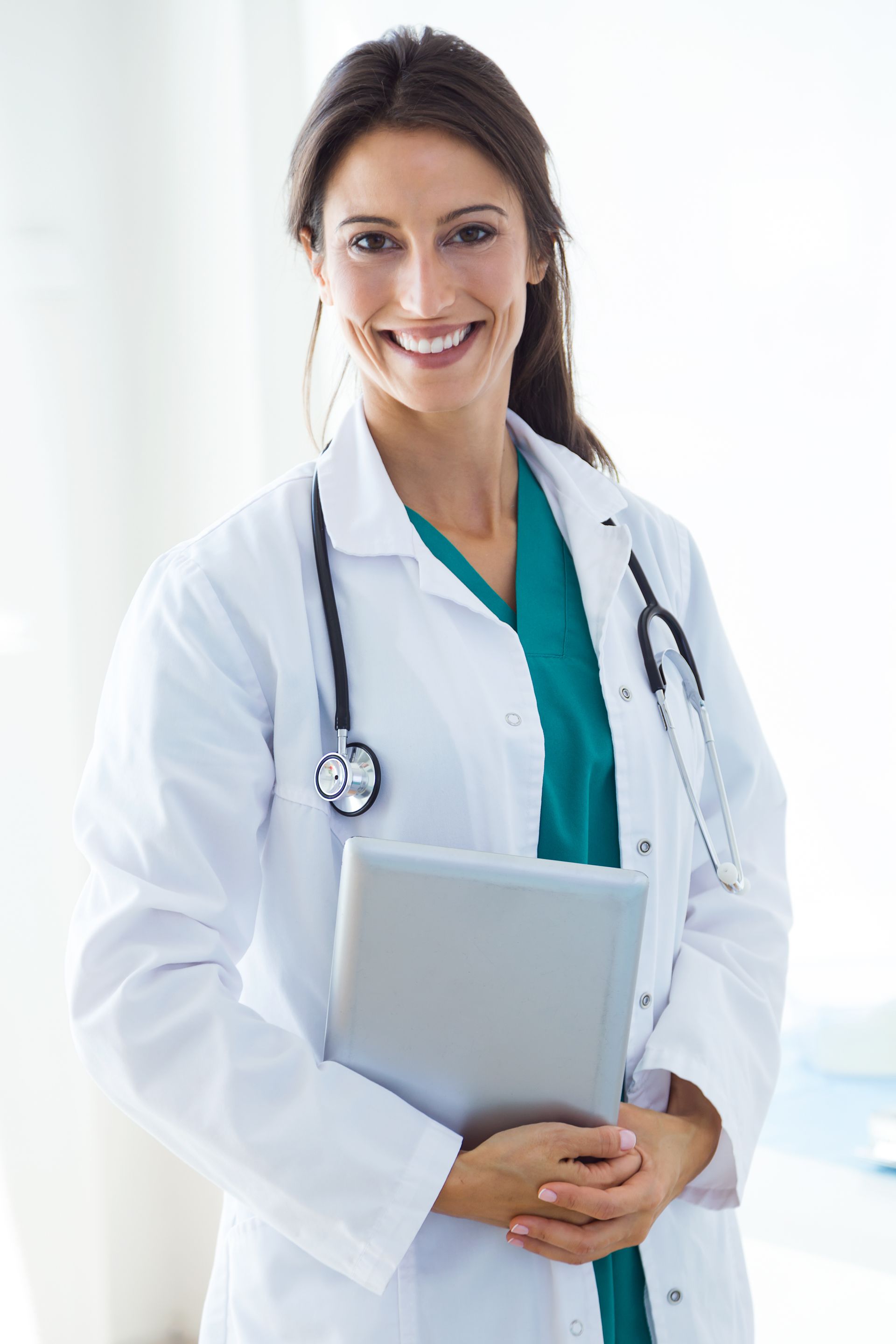 Woman doctor in white coat smiles, holding a tablet, stethoscope, indoors.