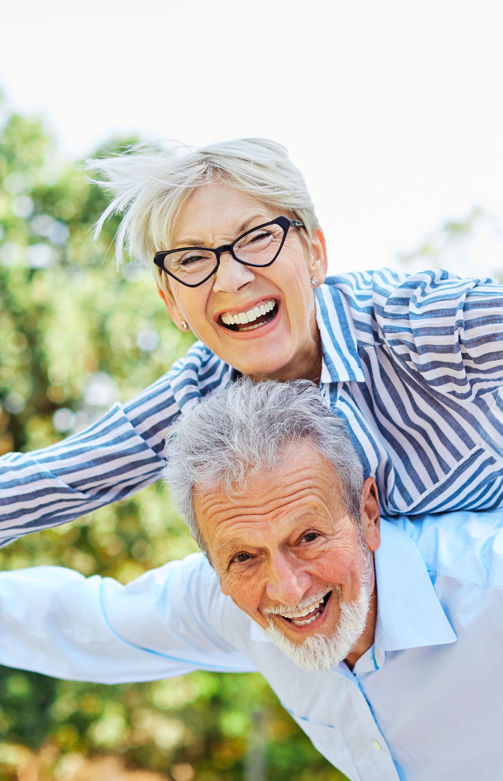 An older man gives a woman a piggyback ride outdoors; both are smiling and laughing.
