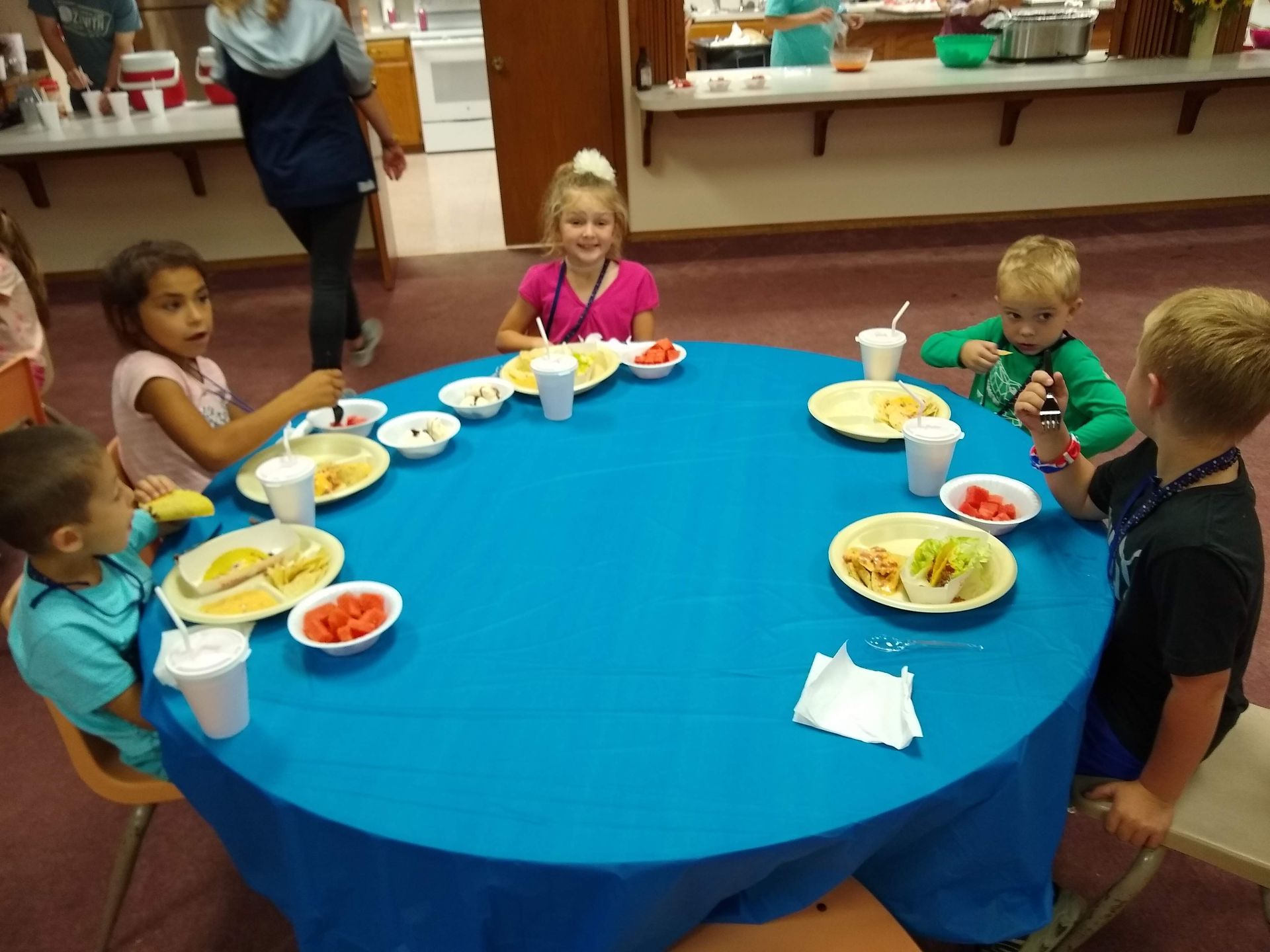 A group of children are sitting around a table with plates of food on it
