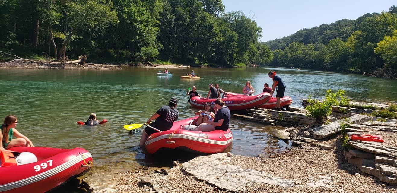 A group of people are sitting in rafts on the shore of a river.
