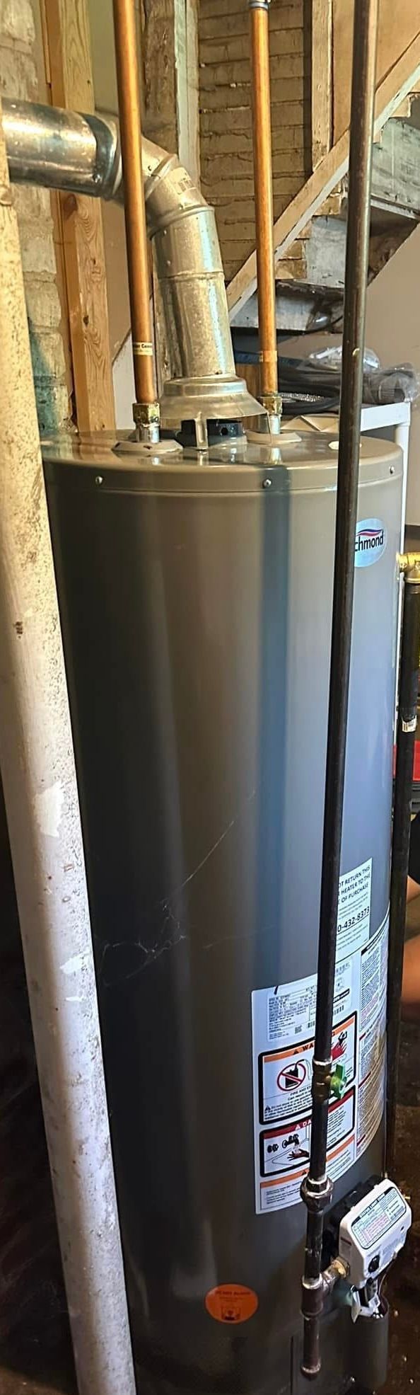 A water heater is sitting in a basement next to a staircase.