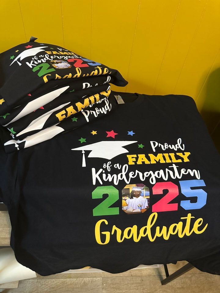 A stack of black shirts that say proud family kindergarten 2025 graduate