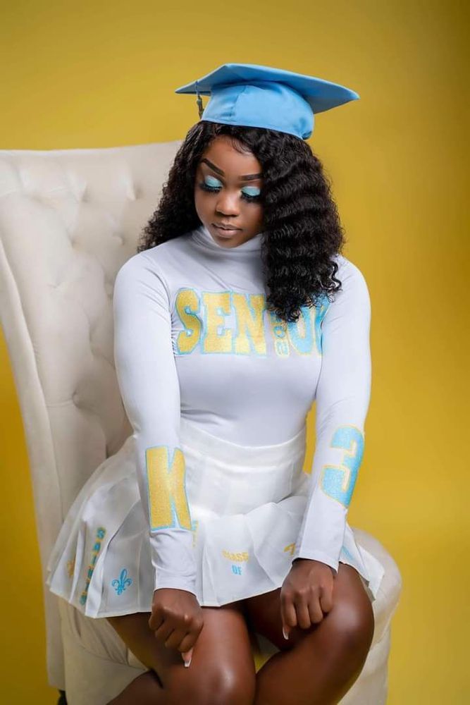 A woman in a graduation cap and gown is sitting in a chair.