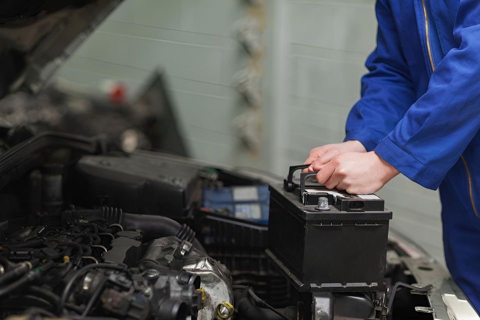 A Mechanic is Working on a Car Battery in a Garage — Cessnock Batteries In Bellbird, NSW
