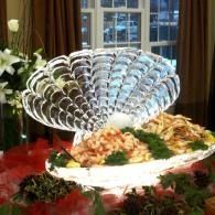 Decorative scalloped fruit and flower display on a table with a banquet spread in the background