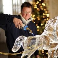 Person pouring molten glass into a horse sculpture in a warmly lit workshop