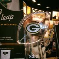 Packers “G” logo football ice sculpture on a clear stand at an indoor event booth