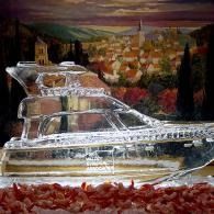 Clear glass boat sculpture on a red surface, with a blurred cityscape painting in the background