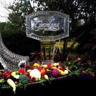 Memorial wreath of colorful flowers beneath a glass plaque in a garden setting