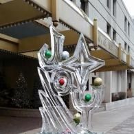 Abstract metallic sculpture with colorful spheres outside a building with the word JOY sculpted in ice.