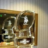 Glass awards with a white logo displayed on a shelf, one large plaque in front and another behind it