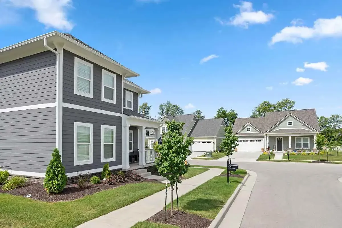A suburban street with a grey two-story house in the foreground and other homes under a clear blue sky.