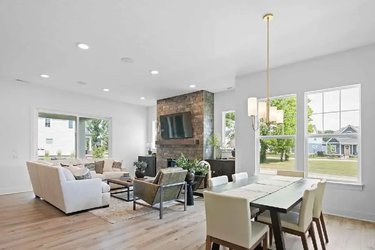 A bright, open-plan living and dining area with a stone fireplace, beige sofa, green armchair, and a dining table.