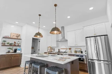 A modern kitchen featuring white cabinets, a central island with bar stools, stainless steel appliances, and pendant lights.