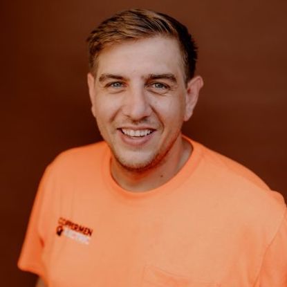 A smiling person wearing an orange shirt with 