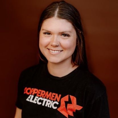 A smiling person with long dark hair wearing a black t-shirt with orange 