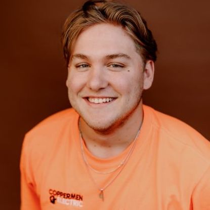 A person with light-brown hair smiles while wearing an orange t-shirt with the CopperMen Electric logo.