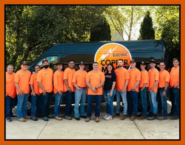 A group of workers in matching orange shirts stand in front of a Copper Electric van parked outdoors.
