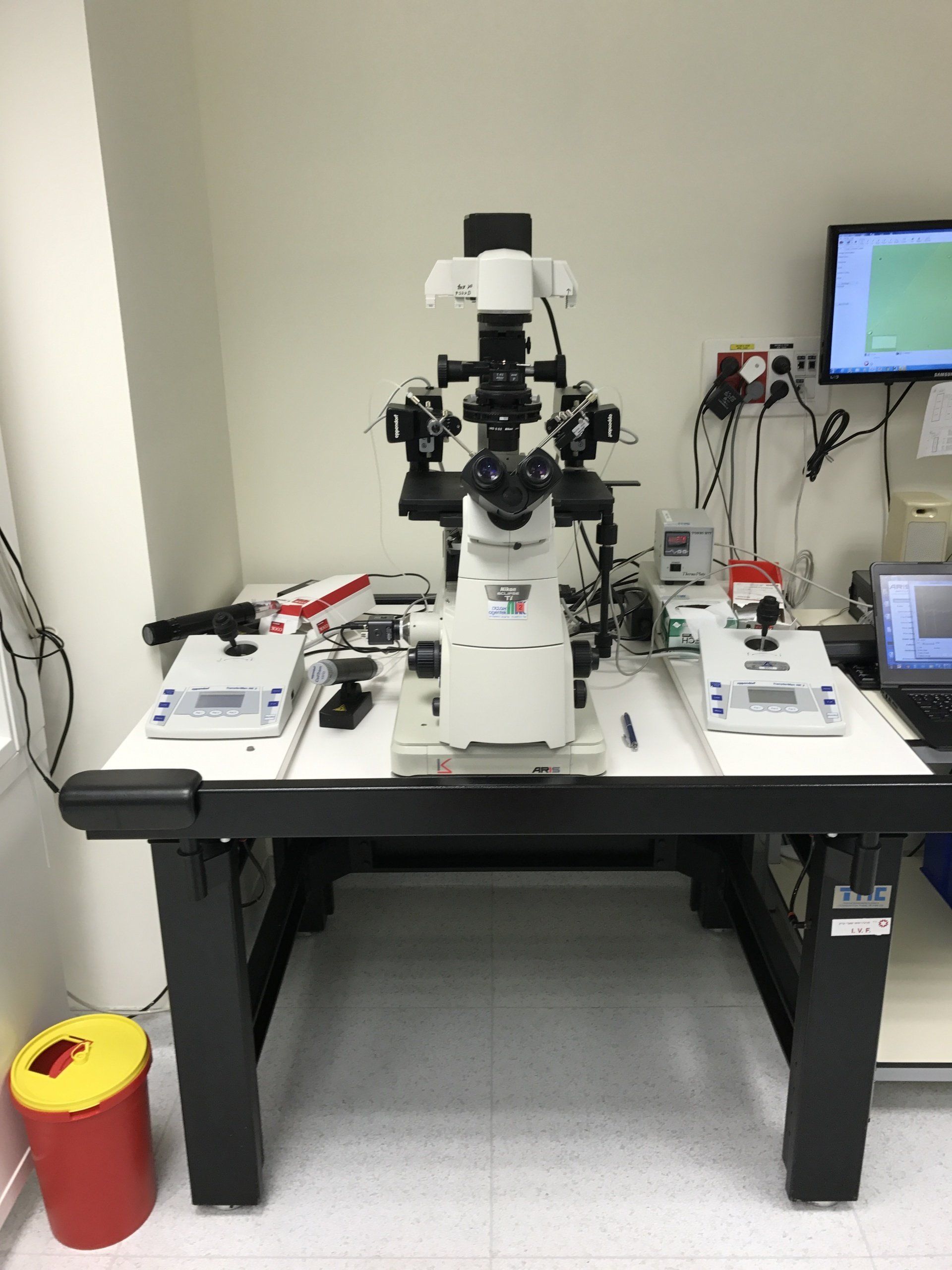 Laboratory microscope on an ARIS vibration isolation platform, flanked by control panels on a sturdy workstation