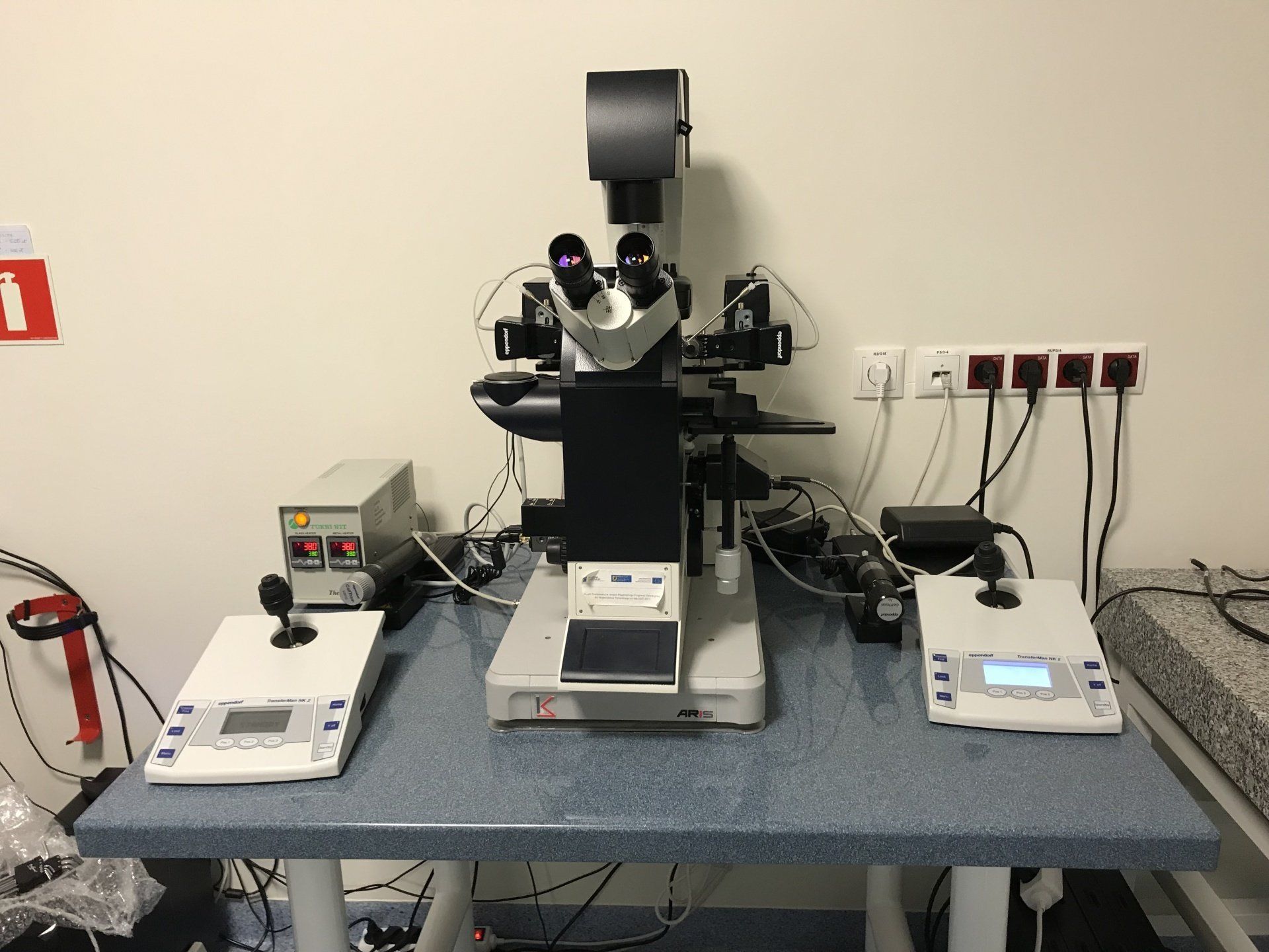 Laboratory microscope setup on an ARIS vibration isolation platform, flanked by two control panels organized on a lab bench