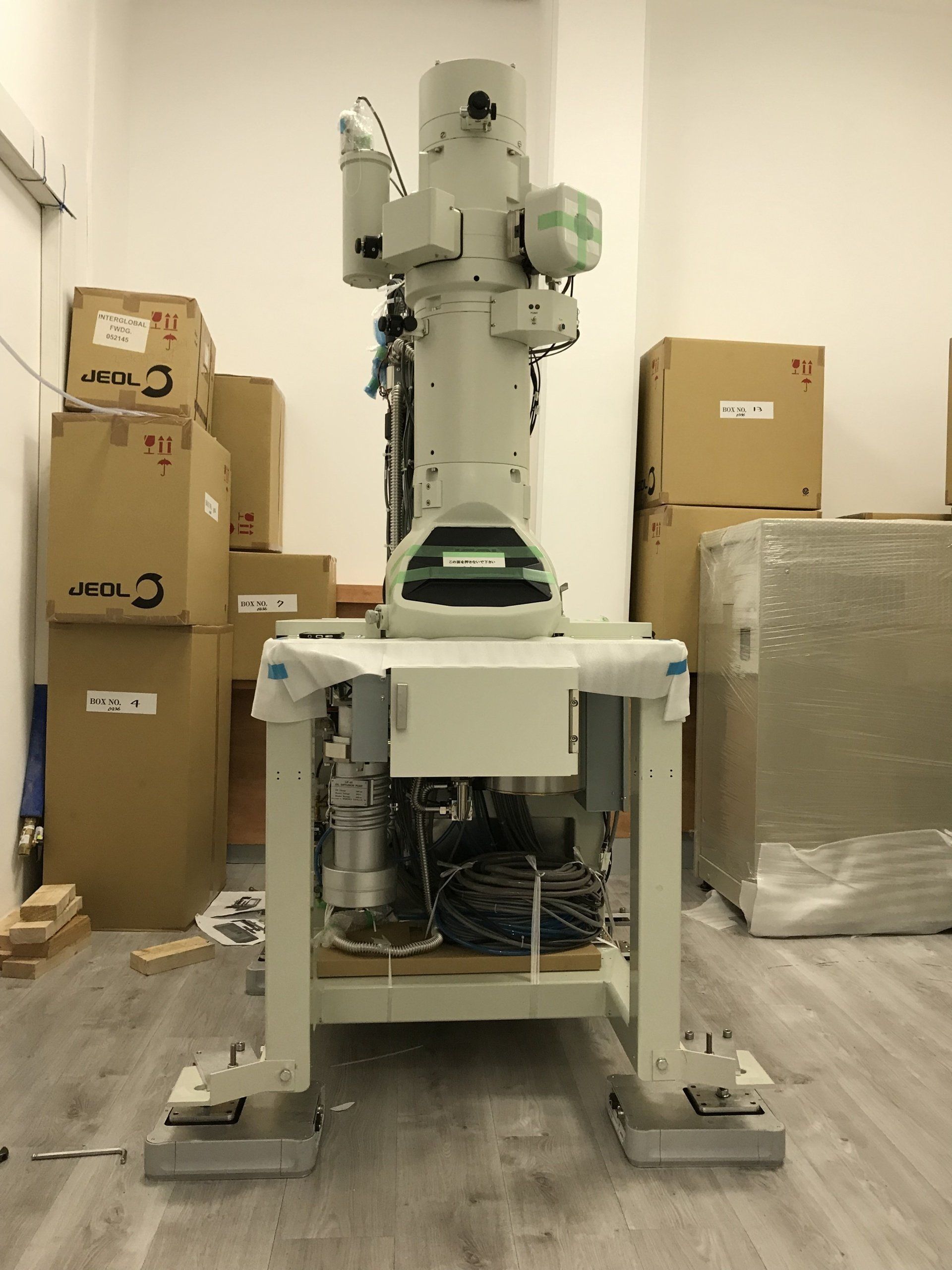 Large laboratory equipment surrounded by labeled JEOL boxes in a storage or setup area