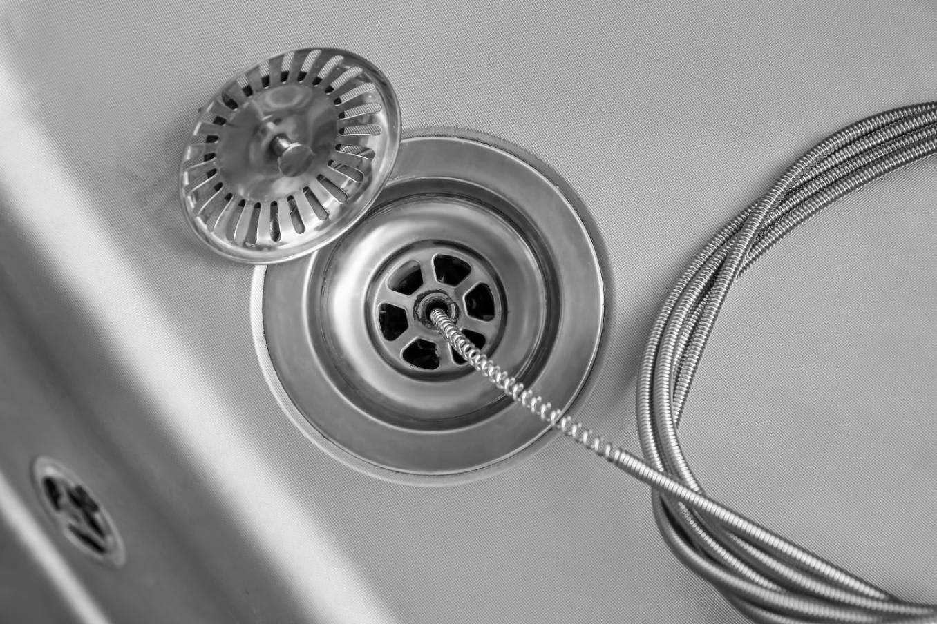 Stainless steel sink drain with plug and strainer, with a coiled cable nearby