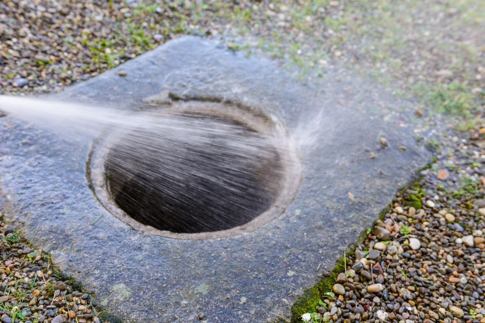 Water flowing into a circular drain hole in a concrete slab with gravel around it