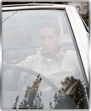 man behind windscreen sat in driving seat of a car