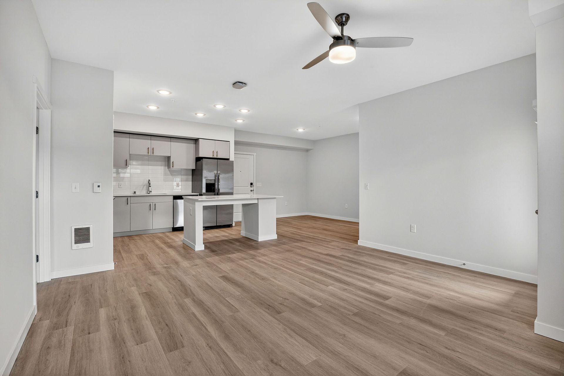 Open-concept apartment with gray walls, wood-look floors, and a kitchen with an island.