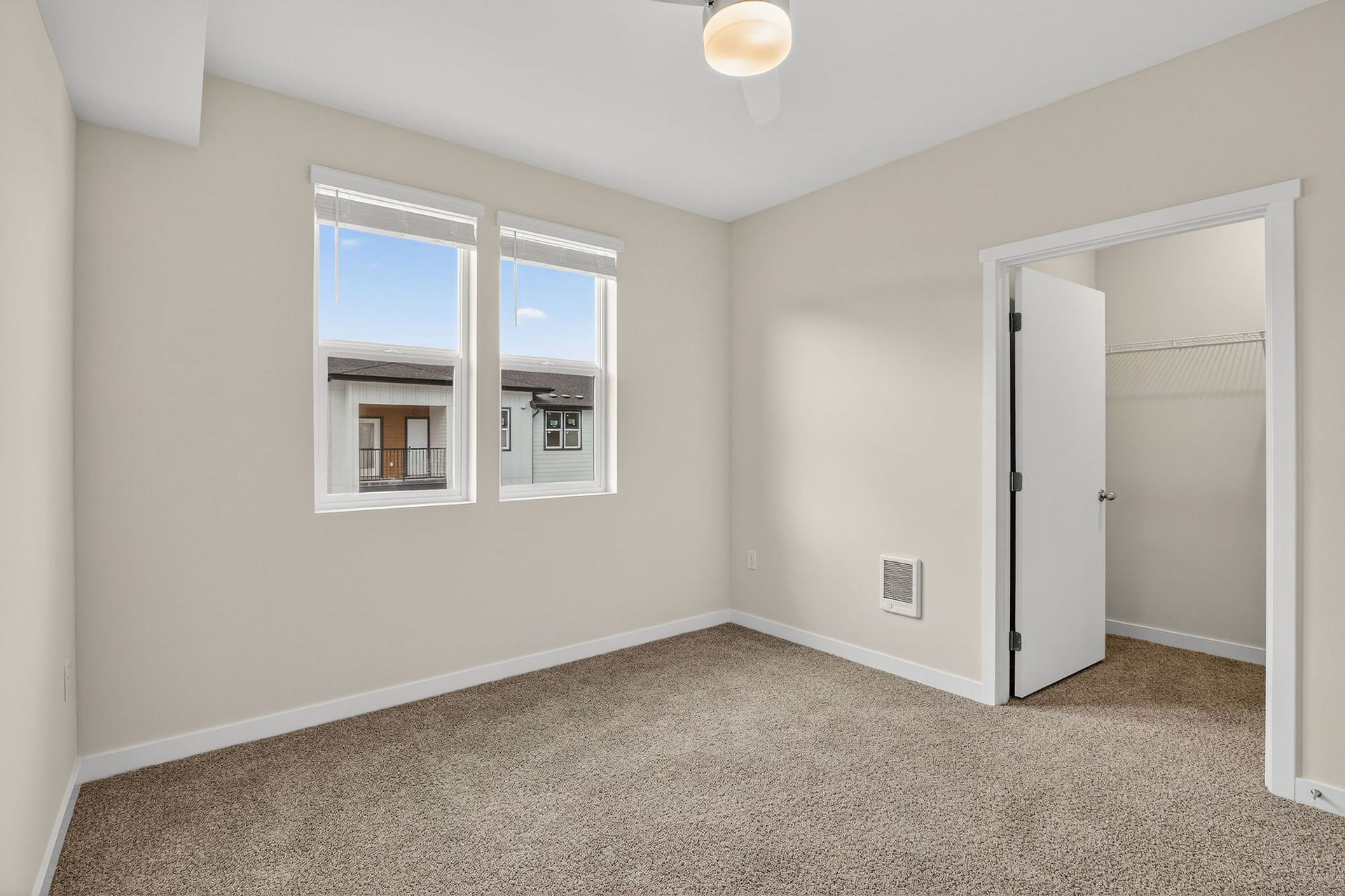 Empty bedroom with two windows, a closet, and beige carpet.