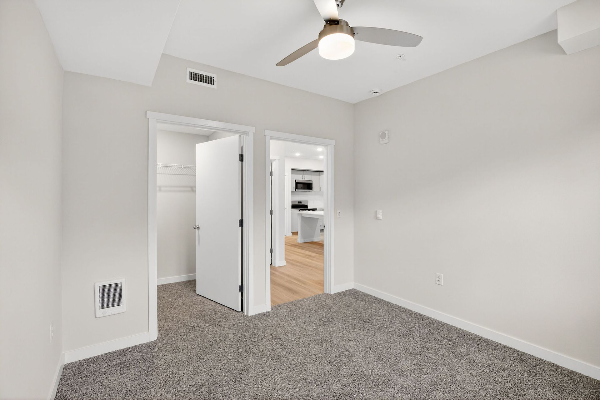 Empty bedroom with gray carpet, a closet, and an open doorway to a kitchen.