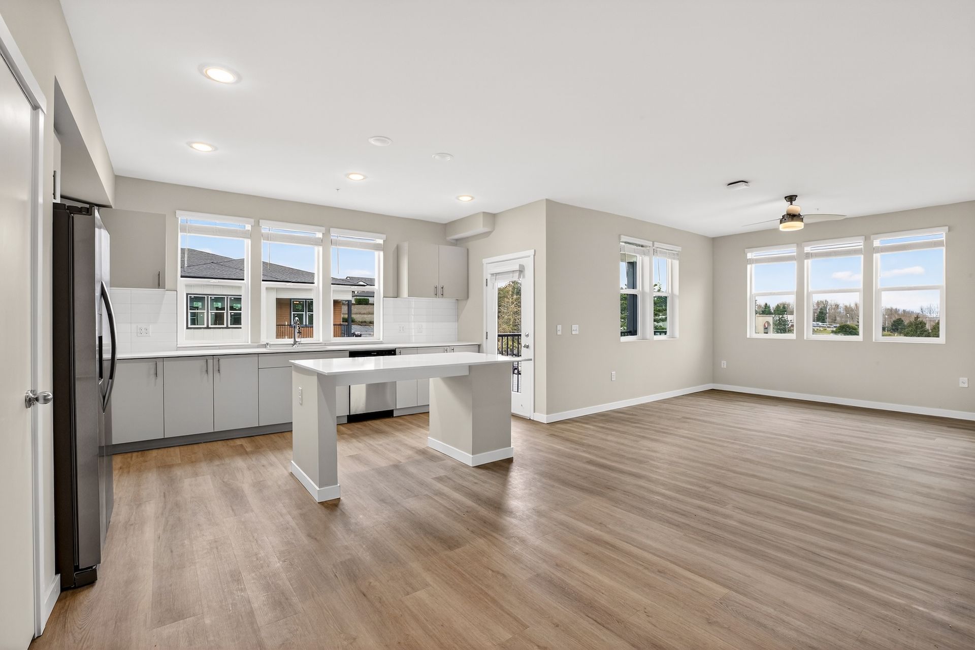 Spacious, bright kitchen and living area with island, windows, and light gray cabinets and walls.