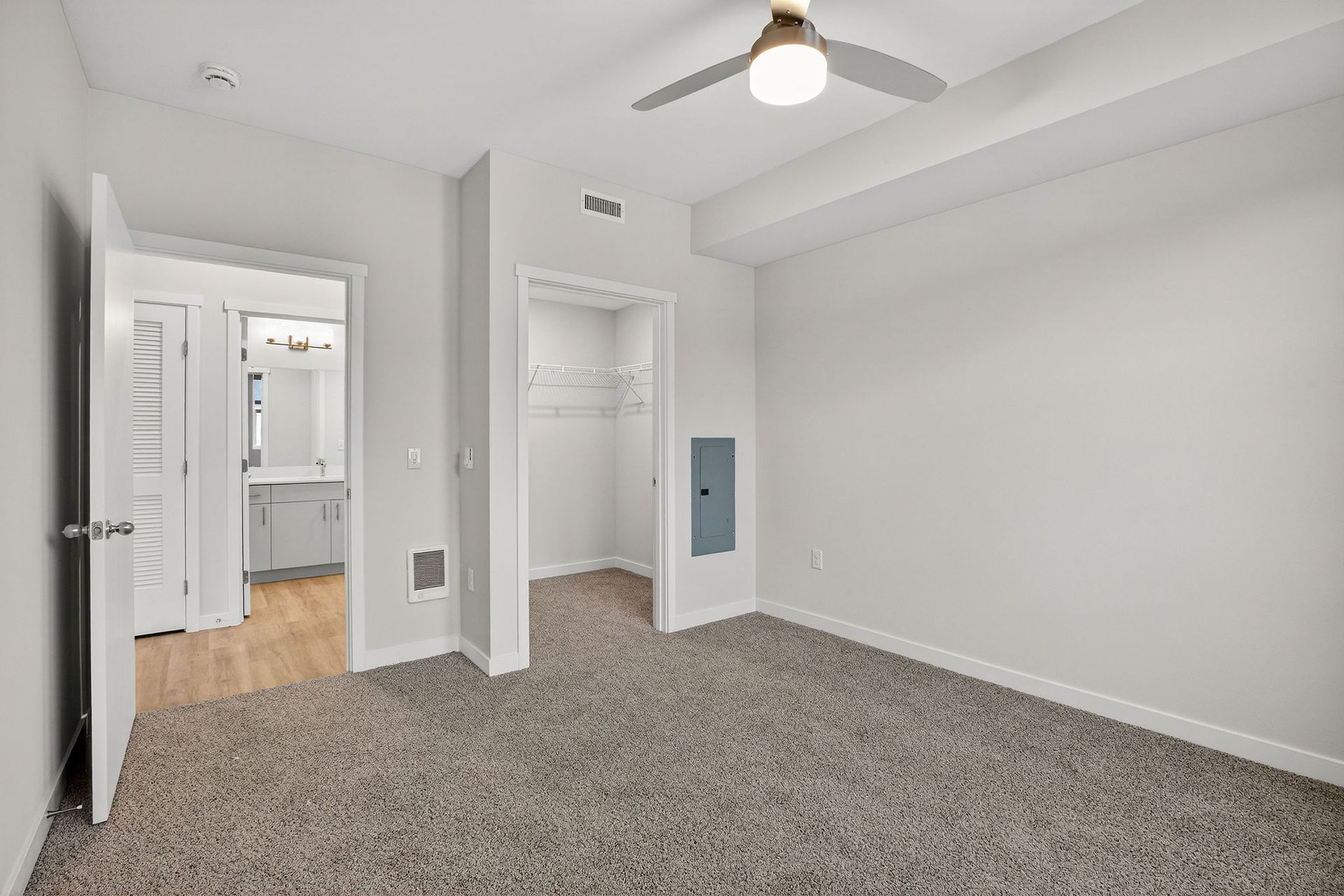 Empty bedroom with gray carpet, white walls, and open doors to a bathroom and closet.