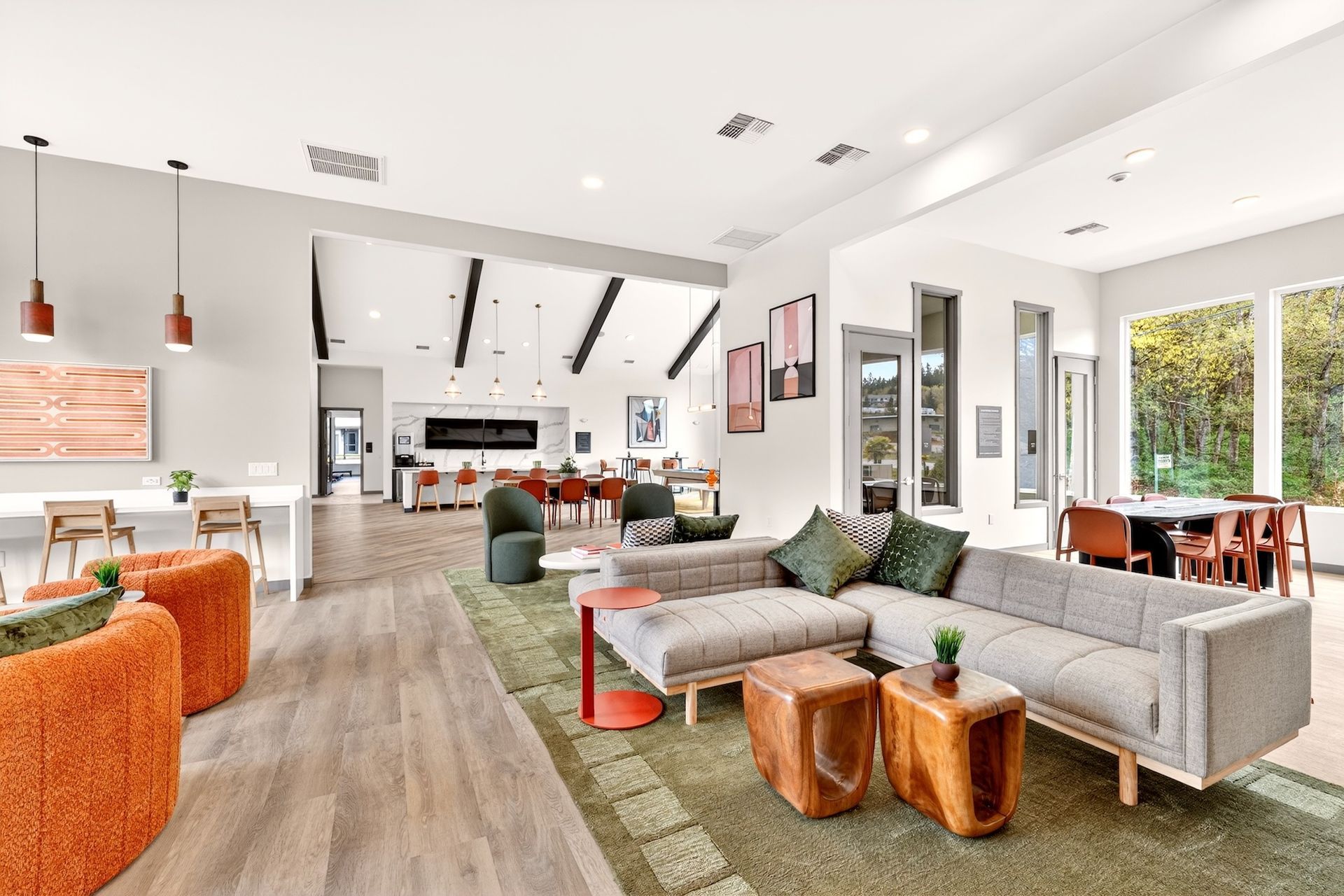 Bright modern living room with gray sectional, orange chair, green rug, and open kitchen dining area