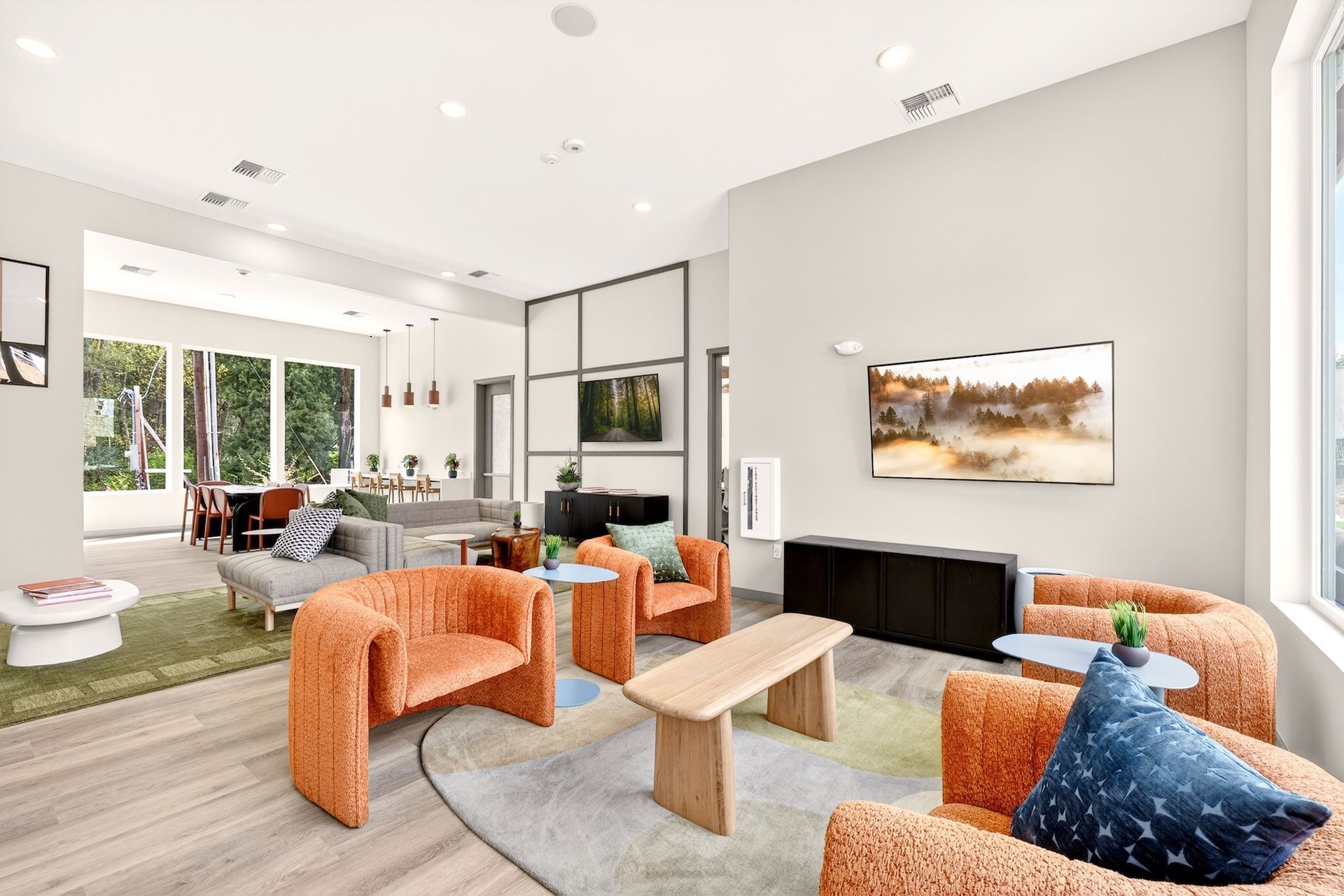 Bright modern living room with orange chairs, gray sofa, wall art, and dining area by large windows