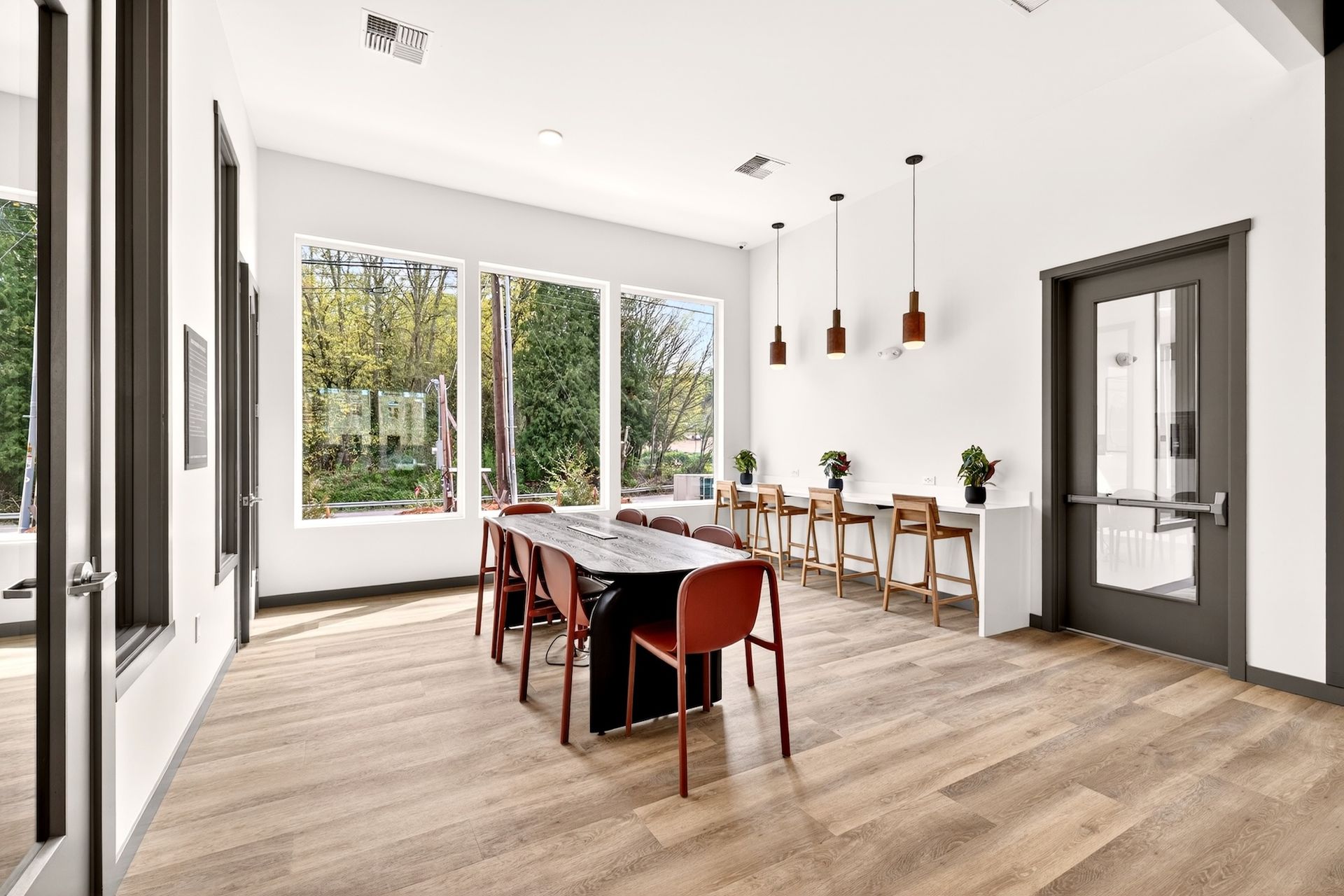 Bright modern dining room with large windows, a long table, chairs, and wood flooring