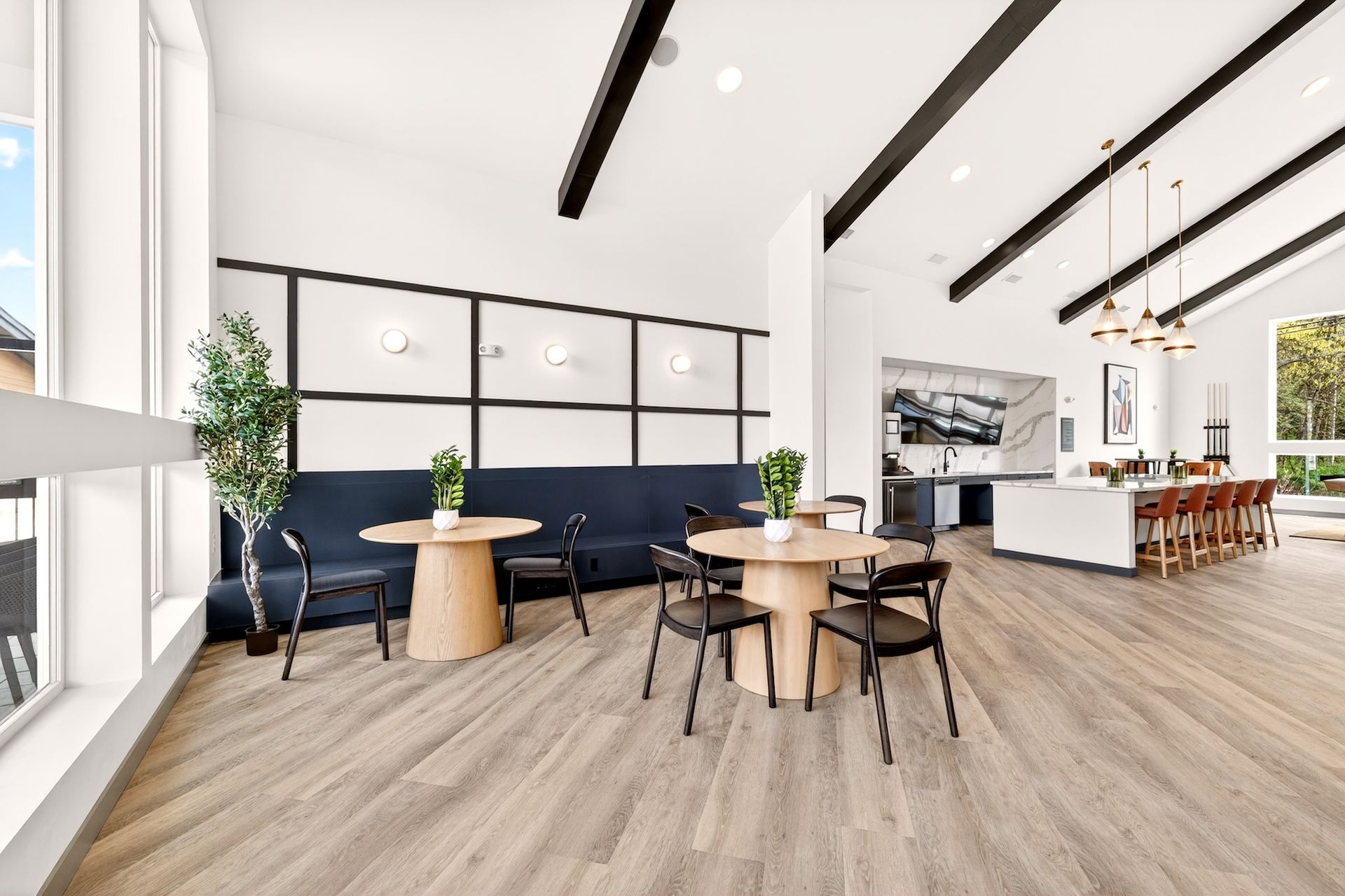 Modern office lounge with blue sofas, round tables, black chairs, and large windows in a bright open space