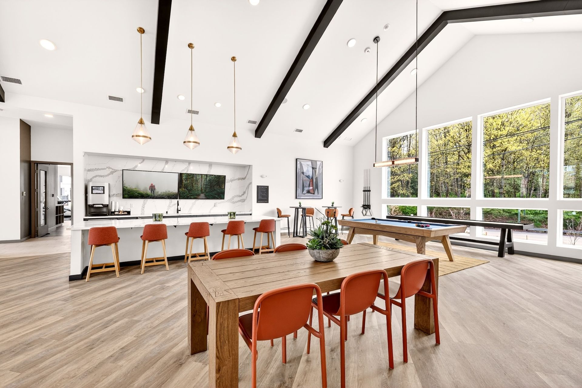 Bright modern dining room with long wooden table, orange chairs, and large windows overlooking greenery