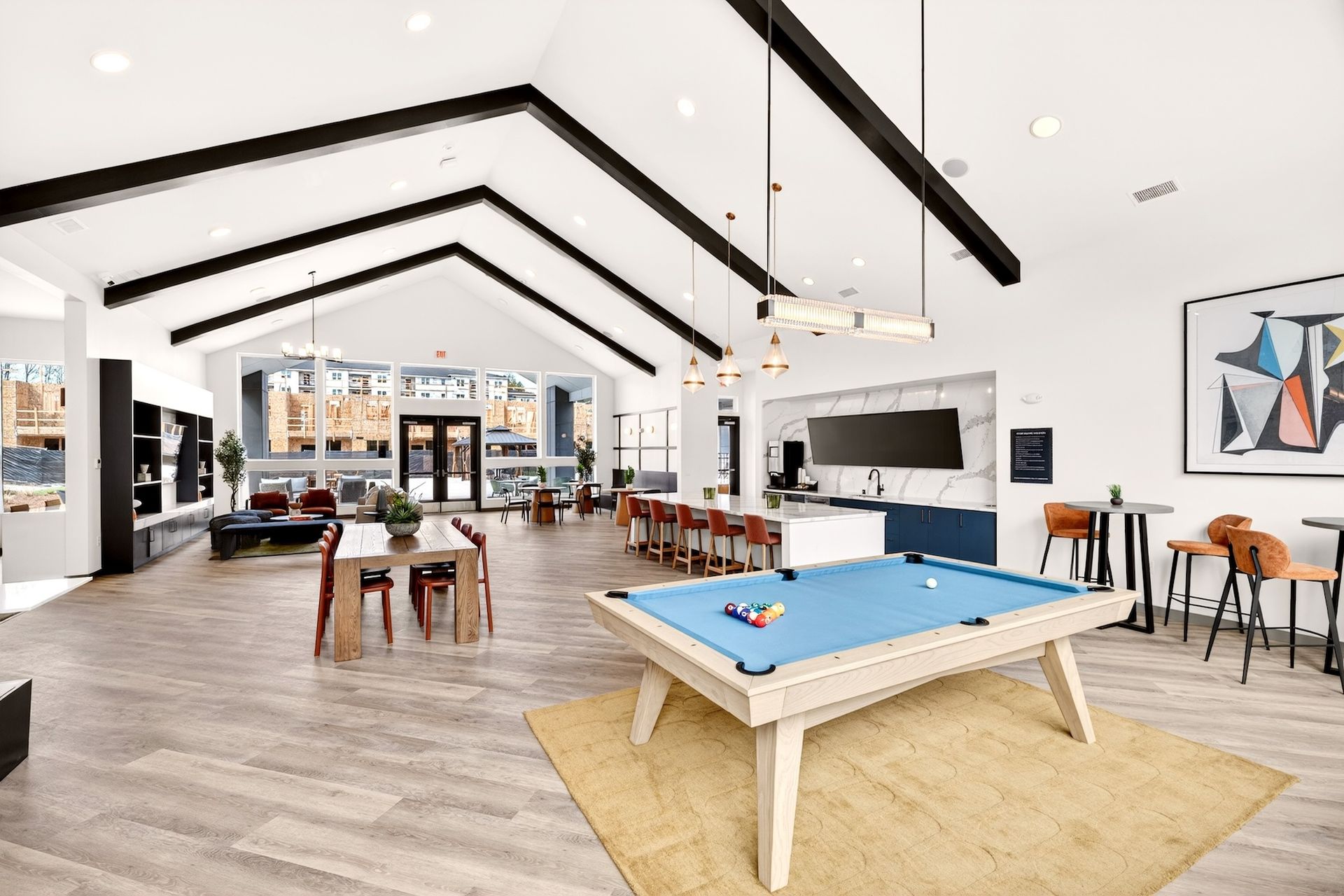 Bright modern game room with pool table, foosball, lounge seating, and exposed black ceiling beams