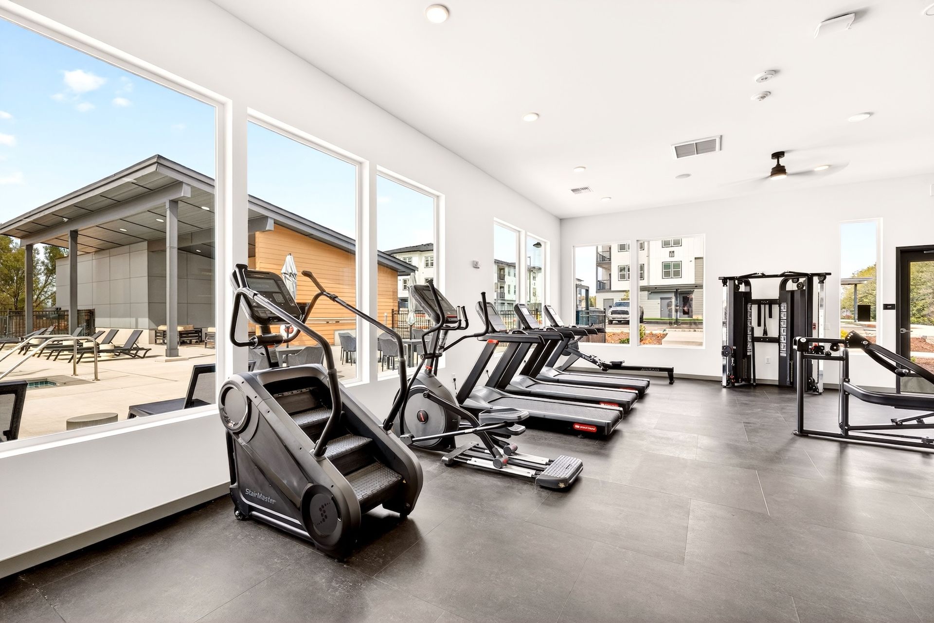 Modern gym interior with treadmills, ellipticals, and large windows overlooking an outdoor patio