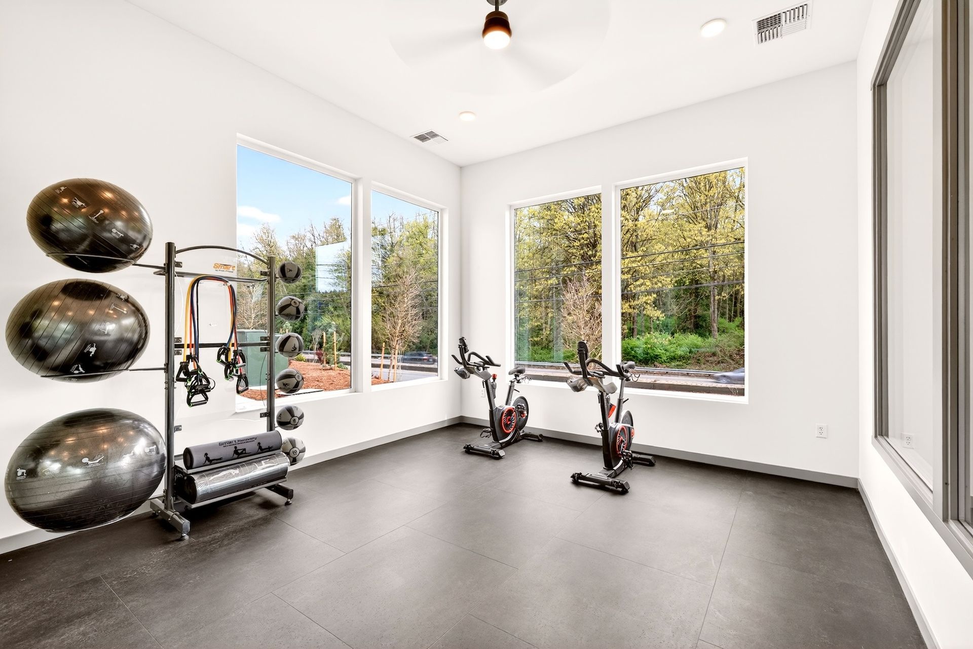 Bright home gym with exercise bikes, weights, and large windows overlooking trees.