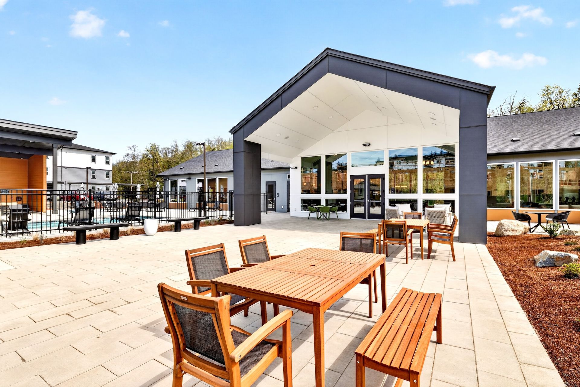 Outdoor café patio with wooden tables and benches beside a modern building on a sunny day