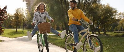 Couple biking on a path in a park; the woman is excited and has her legs out.